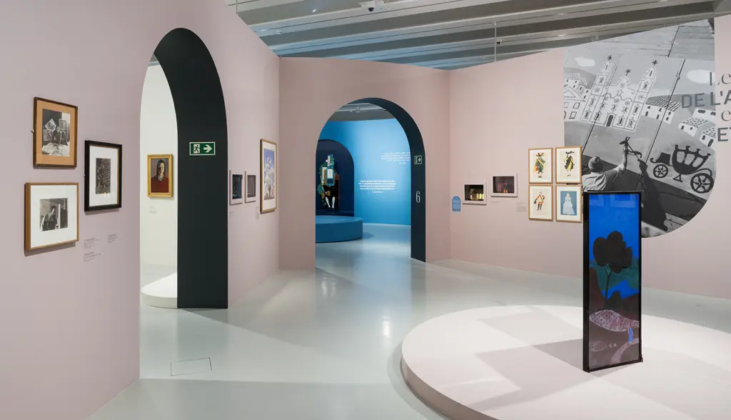 Dans une salle d'exposition aux murs couleur vieux rose, plusieurs œuvres sont exposées, dont un paravent. Sur le mur de droite, une grand photo noir & blanc montre Jean Hugo devant un de ses décors de théâtre, un carosse devant un château. Dans le mur du fond et celui de gauche, deux arches ouvrent vers d'autres salles d'exposition.